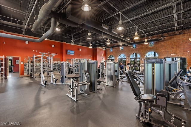 gym featuring a towering ceiling, brick wall, and track lighting