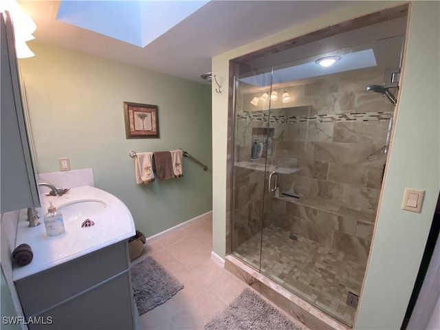bathroom featuring tile patterned flooring, a skylight, vanity, baseboards, and a shower stall