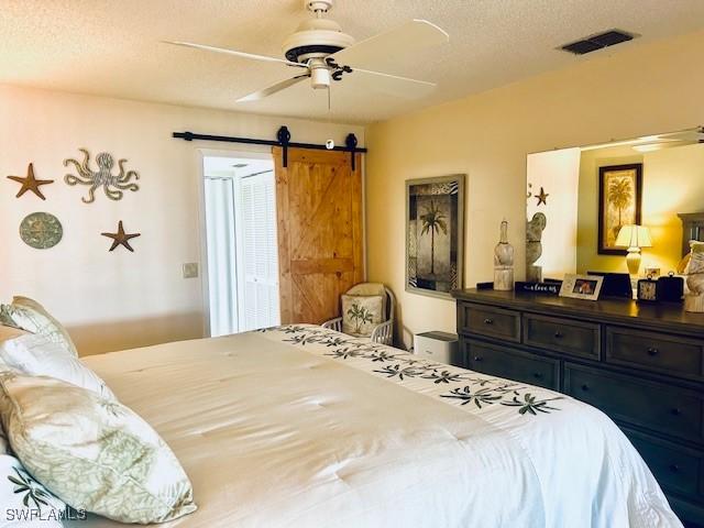 bedroom with visible vents, ceiling fan, a textured ceiling, and a barn door