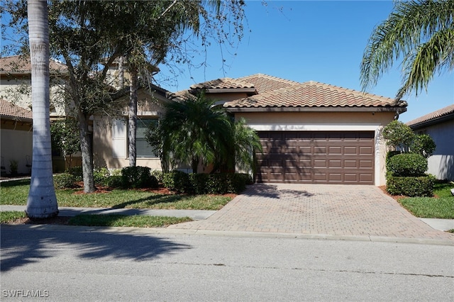 view of front of house with decorative driveway, a tile roof, an attached garage, and stucco siding