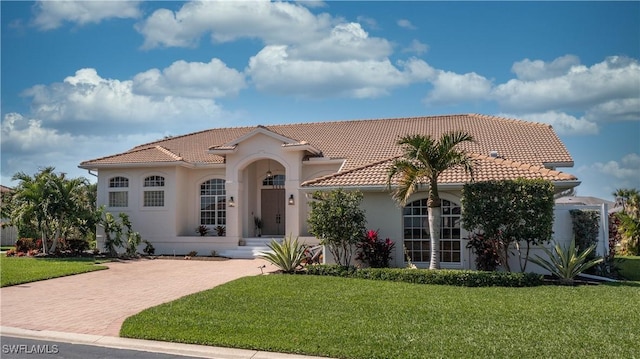 mediterranean / spanish-style house with decorative driveway, a front yard, a tile roof, and stucco siding