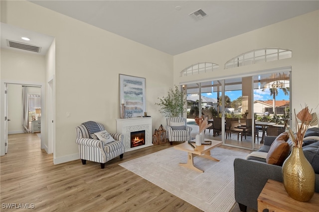living room with a towering ceiling, visible vents, and a warm lit fireplace