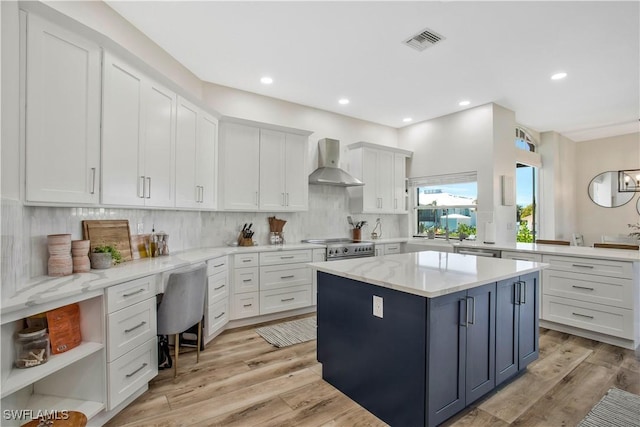 kitchen featuring light wood-style flooring, a kitchen island, visible vents, white cabinetry, and wall chimney range hood