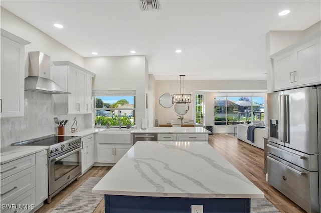 kitchen featuring a center island, visible vents, white cabinetry, wall chimney range hood, and high quality appliances