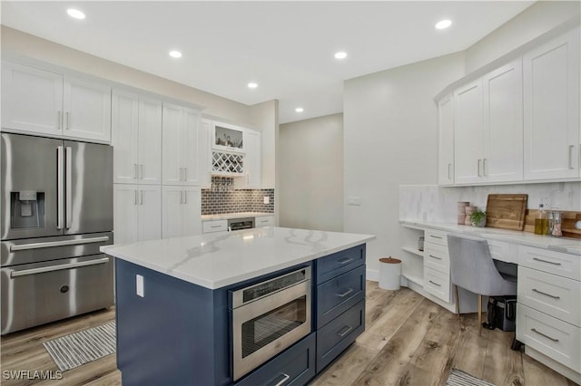 kitchen featuring light stone countertops, white cabinets, appliances with stainless steel finishes, light wood-type flooring, and a center island