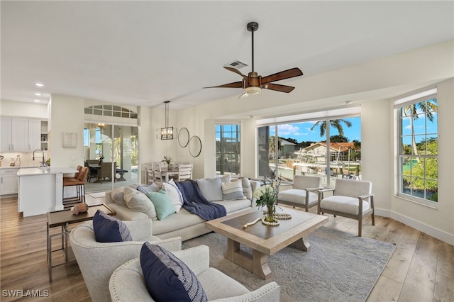 living area featuring recessed lighting, baseboards, visible vents, light wood-style floors, and ceiling fan with notable chandelier