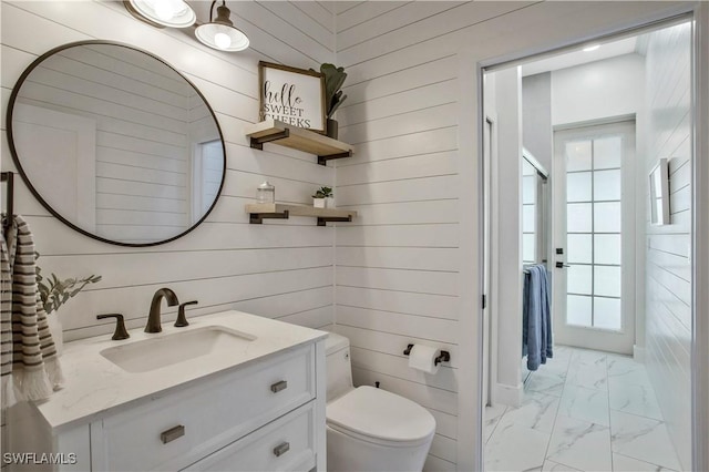 bathroom featuring toilet, wood walls, marble finish floor, and vanity