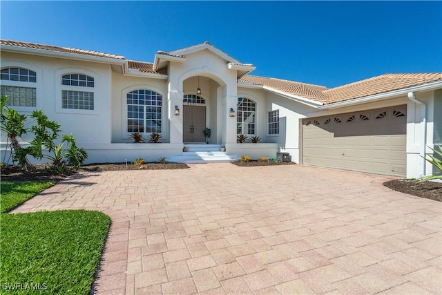 mediterranean / spanish house with an attached garage, stucco siding, decorative driveway, and a tiled roof