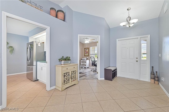 entrance foyer with ceiling fan with notable chandelier, vaulted ceiling, baseboards, and light tile patterned floors