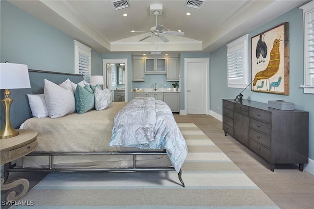 bedroom with light wood-style flooring, a raised ceiling, and visible vents