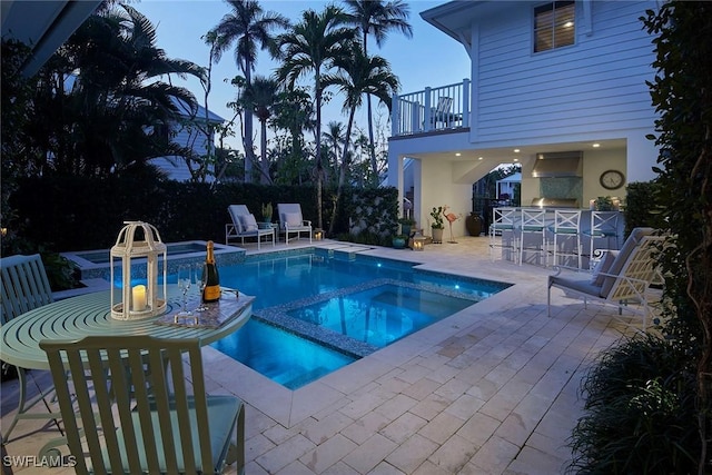 pool at dusk with a patio area, a pool with connected hot tub, and an outdoor bar