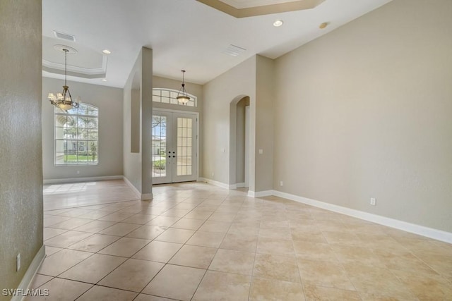 tiled empty room featuring a notable chandelier, ornamental molding, a raised ceiling, and french doors