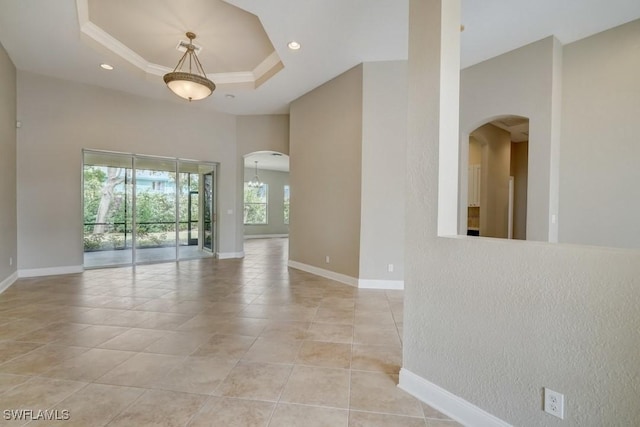 spare room with a tray ceiling, crown molding, a high ceiling, and light tile patterned floors