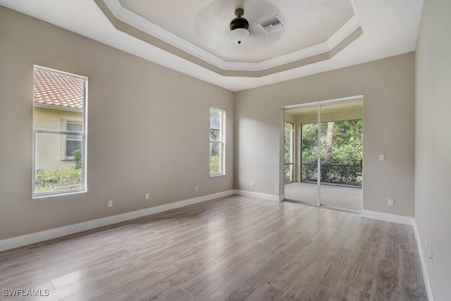 spare room with a tray ceiling, ornamental molding, a healthy amount of sunlight, and light hardwood / wood-style flooring