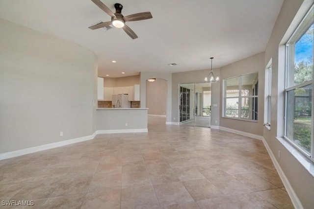 unfurnished living room with light tile patterned floors, a wealth of natural light, and ceiling fan with notable chandelier