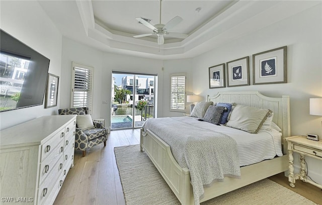 bedroom with ceiling fan, access to outside, a raised ceiling, and light wood-style flooring