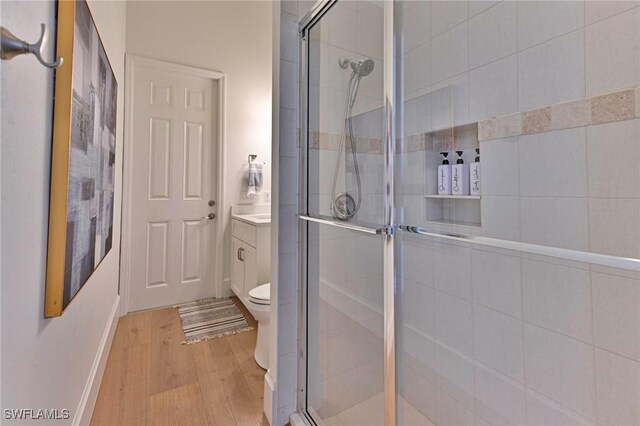 bathroom with toilet, a shower stall, wood finished floors, and vanity