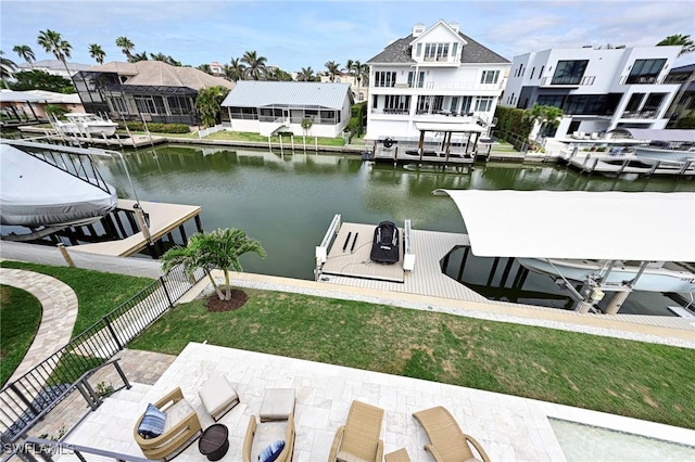 view of dock with boat lift, a water view, fence, a lawn, and a residential view