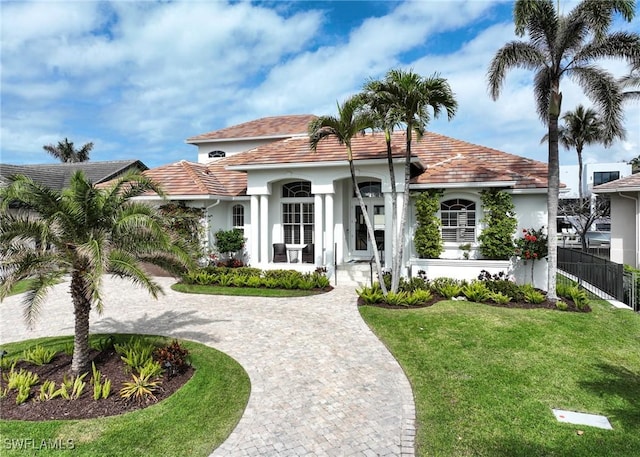 mediterranean / spanish-style house with fence, a tile roof, driveway, stucco siding, and a front yard