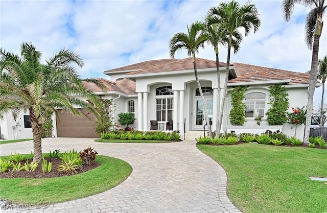 mediterranean / spanish house with a garage, stucco siding, decorative driveway, and a front yard