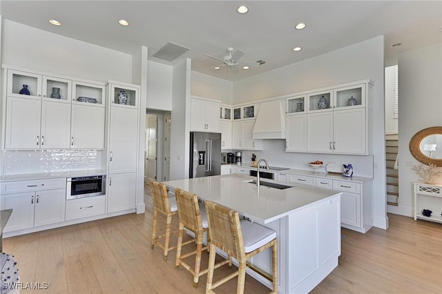 kitchen featuring light countertops, white cabinets, a kitchen island with sink, premium range hood, and high end refrigerator