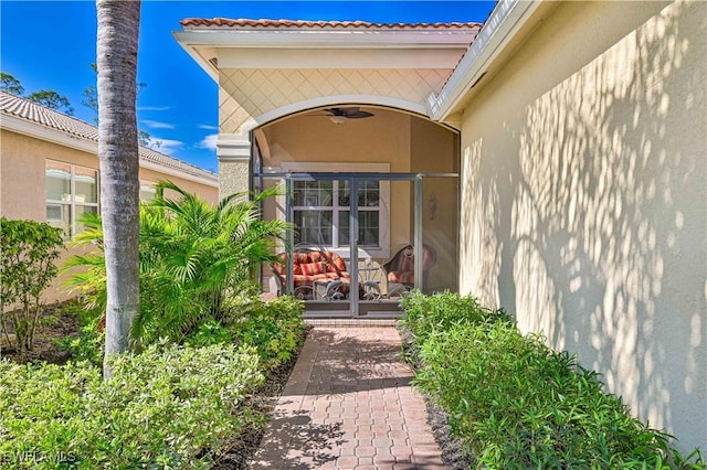 entrance to property with a tile roof, a ceiling fan, and stucco siding