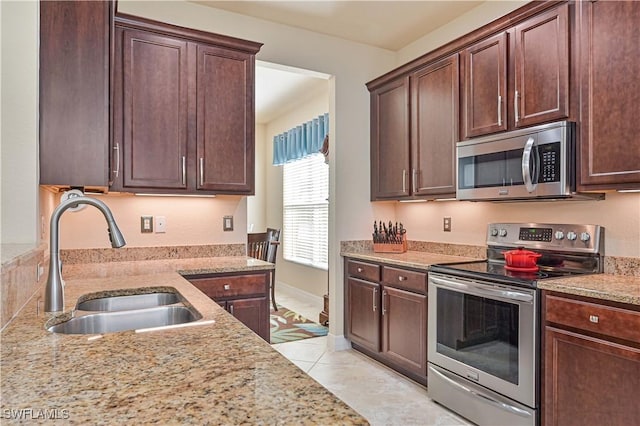 kitchen featuring stainless steel appliances, light stone counters, a sink, and dark brown cabinets