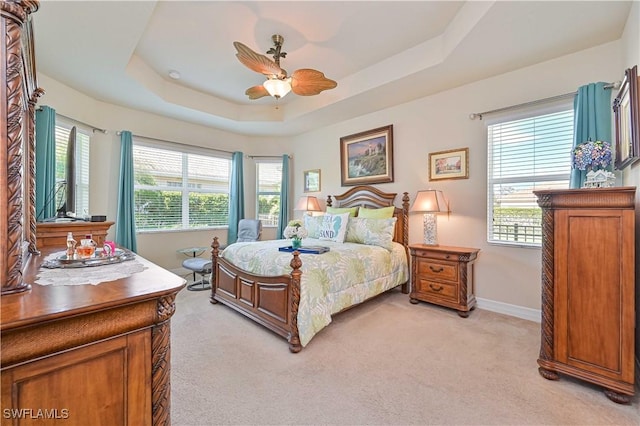 bedroom featuring baseboards, a tray ceiling, a ceiling fan, and light colored carpet