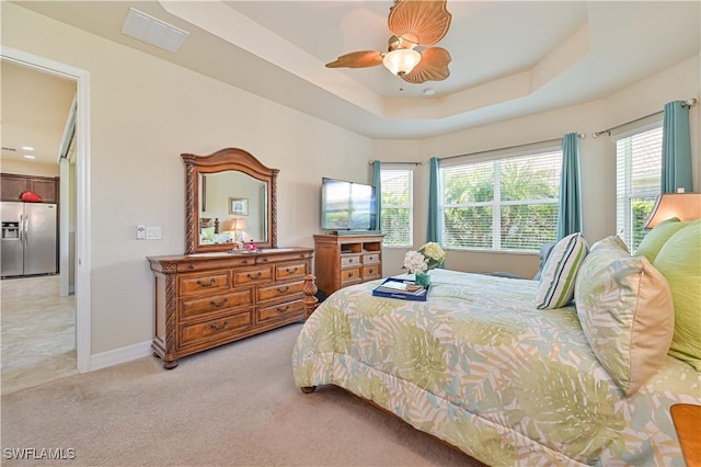 bedroom with a raised ceiling, multiple windows, stainless steel fridge, and light colored carpet