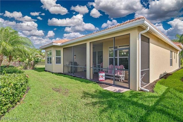 back of house featuring a sunroom, stucco siding, a lawn, and fence