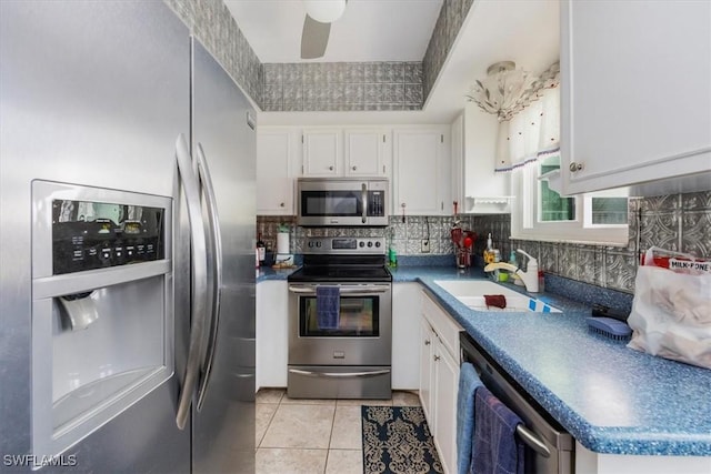 kitchen featuring light tile patterned floors, stainless steel appliances, a sink, white cabinetry, and tasteful backsplash