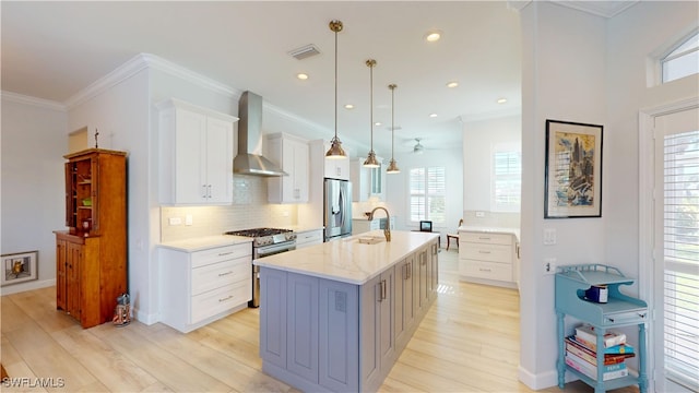 kitchen with appliances with stainless steel finishes, white cabinets, wall chimney range hood, and light wood finished floors