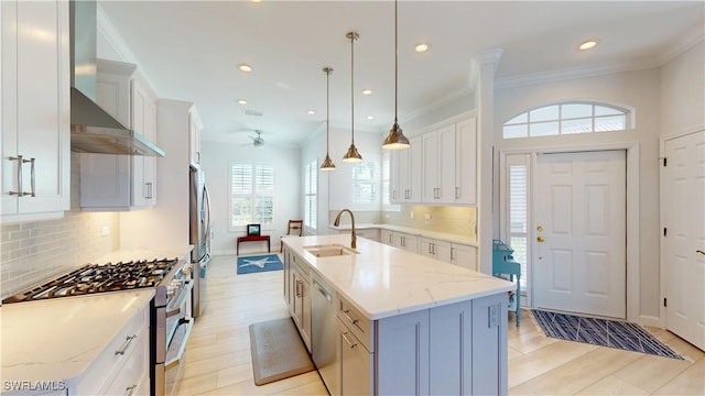 kitchen with appliances with stainless steel finishes, ornamental molding, white cabinetry, a sink, and wall chimney exhaust hood