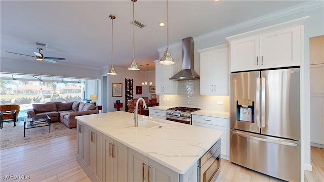 kitchen with decorative backsplash, appliances with stainless steel finishes, a kitchen island with sink, a sink, and wall chimney range hood