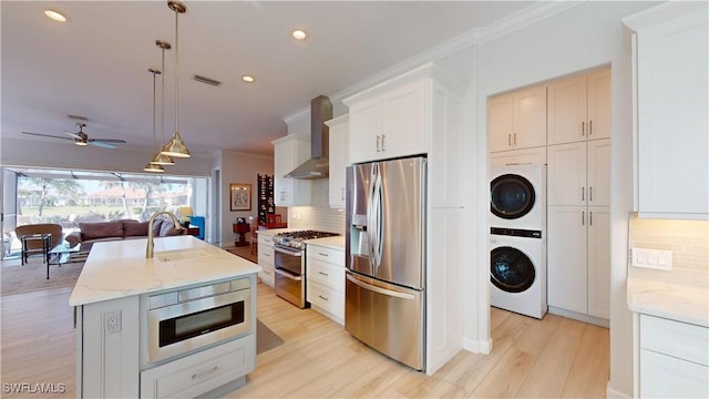 kitchen featuring stacked washer and dryer, appliances with stainless steel finishes, ornamental molding, wall chimney range hood, and a sink