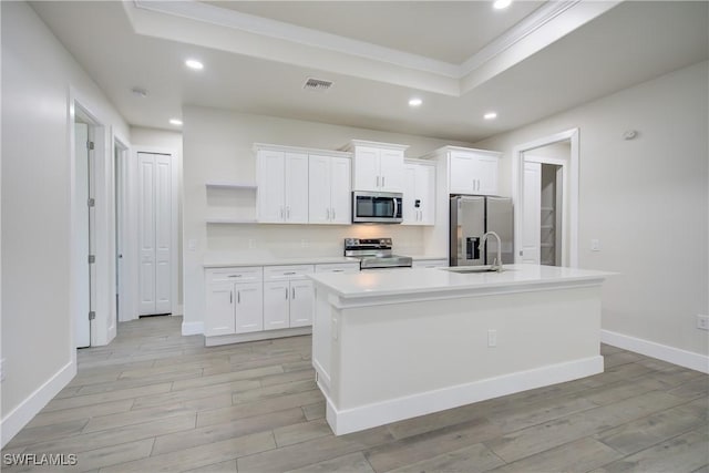 kitchen with a center island with sink, light wood-type flooring, stainless steel appliances, white cabinets, and a raised ceiling