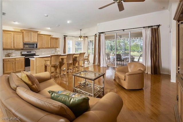 living room with wood finished floors, ornamental molding, visible vents, and ceiling fan