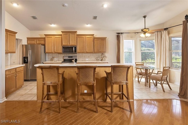 kitchen with brown cabinets, a kitchen island with sink, light countertops, and appliances with stainless steel finishes