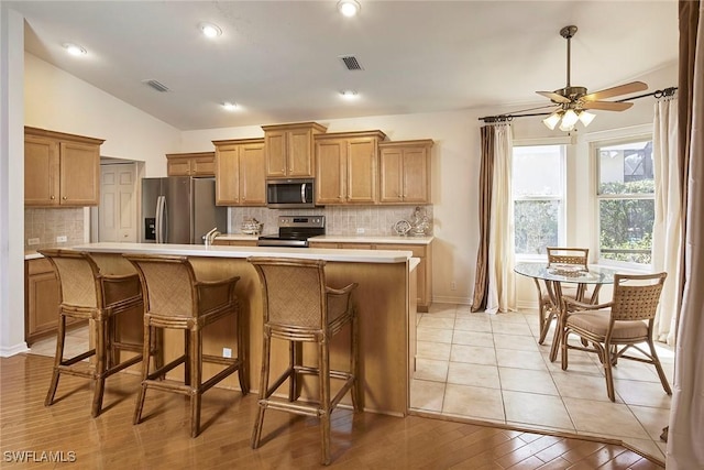 kitchen featuring stainless steel appliances, vaulted ceiling, light countertops, and a center island with sink