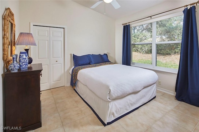 bedroom featuring light tile patterned floors, vaulted ceiling, a closet, baseboards, and a ceiling fan