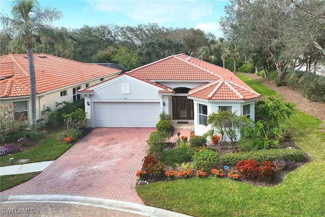 mediterranean / spanish-style house with an attached garage, a tiled roof, decorative driveway, a front lawn, and stucco siding