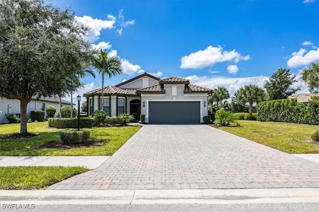 mediterranean / spanish-style home featuring a garage, a tiled roof, decorative driveway, stucco siding, and a front lawn