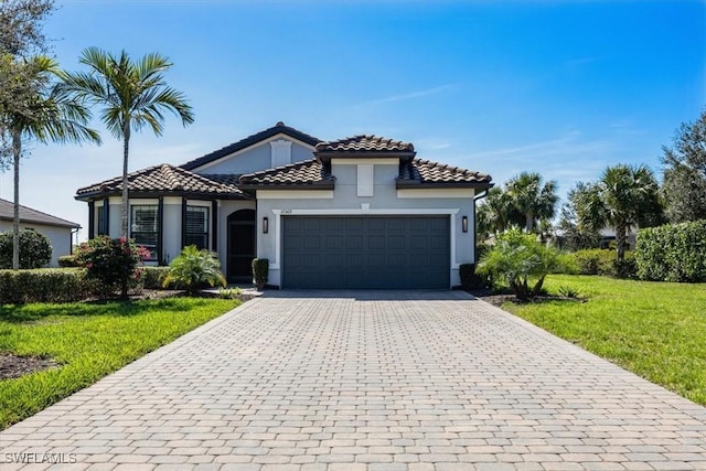 mediterranean / spanish-style home with a garage, a tiled roof, decorative driveway, stucco siding, and a front lawn