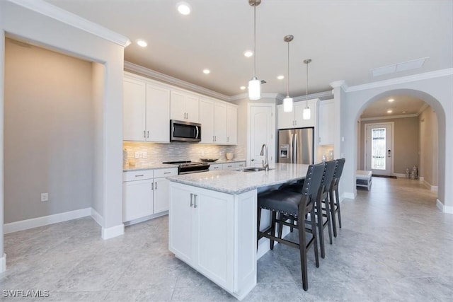 kitchen with arched walkways, tasteful backsplash, appliances with stainless steel finishes, a sink, and a kitchen breakfast bar