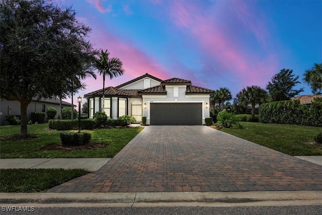 mediterranean / spanish house with decorative driveway, a yard, stucco siding, a garage, and a tiled roof