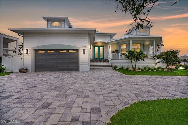 view of front of house with an attached garage, a porch, decorative driveway, and french doors