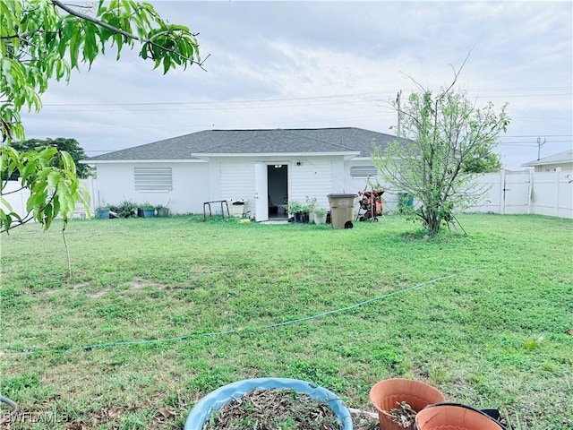 rear view of house featuring a shingled roof, a fenced backyard, and a yard