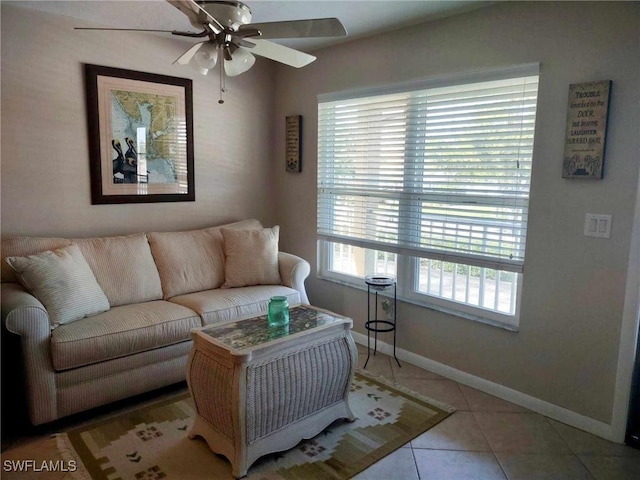 living area with light tile patterned floors, a ceiling fan, and baseboards