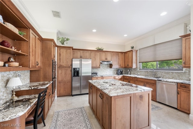 kitchen with a sink, a kitchen island, appliances with stainless steel finishes, light stone countertops, and crown molding