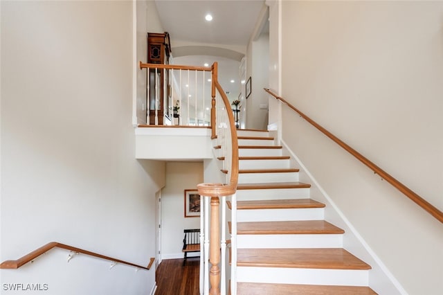 staircase featuring a towering ceiling, baseboards, wood finished floors, and recessed lighting